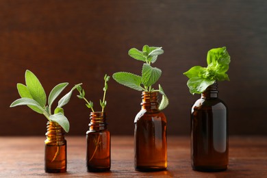 Photo of Bottles of essential oils with fresh herbs on wooden table