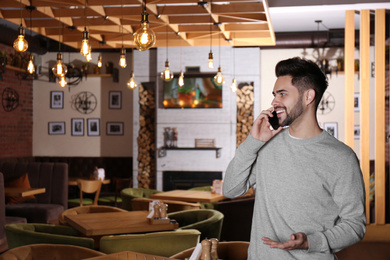 Photo of Young business owner talking on phone in his cafe. Space for text