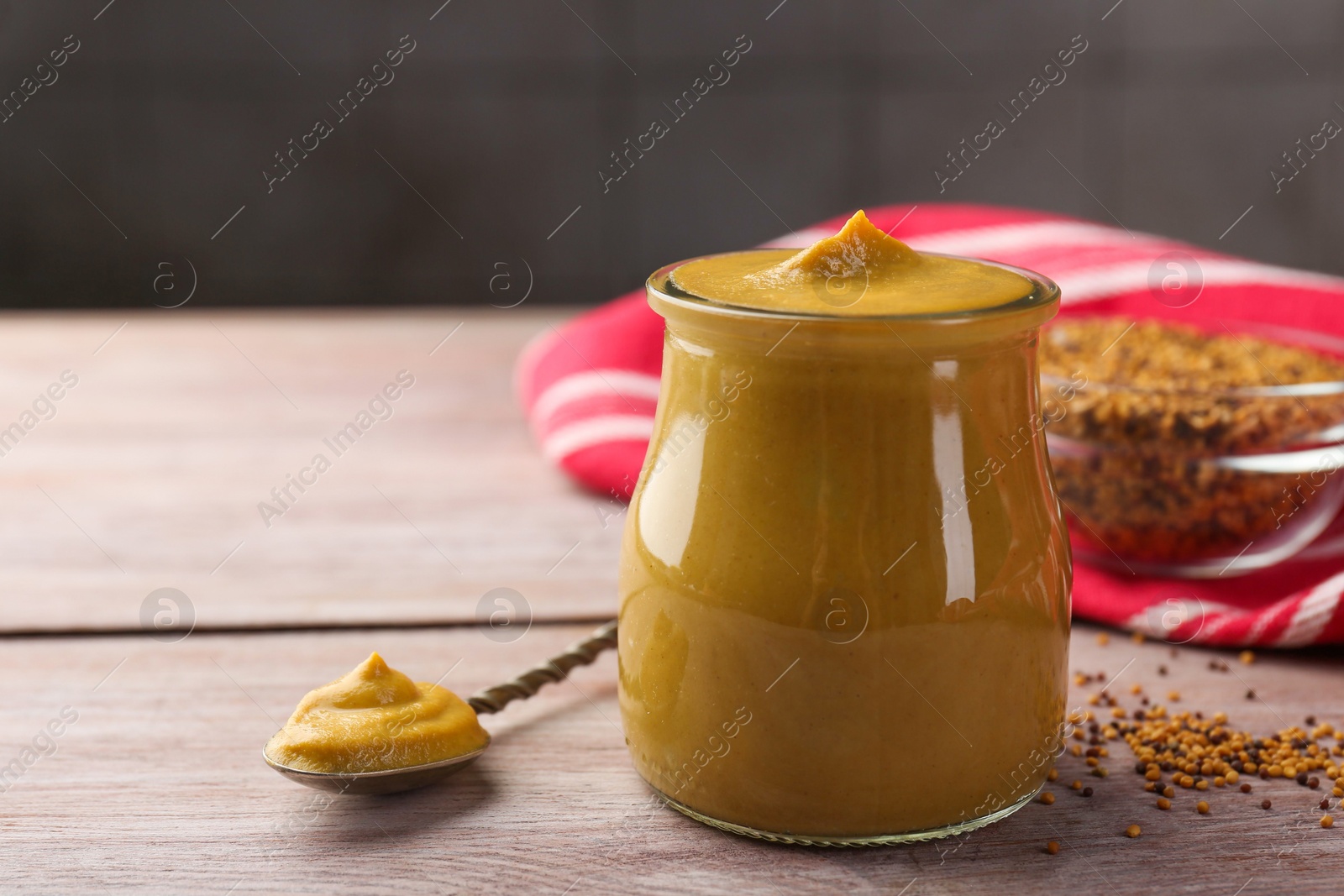 Photo of Jar and spoon with tasty mustard sauce on wooden table, space for text