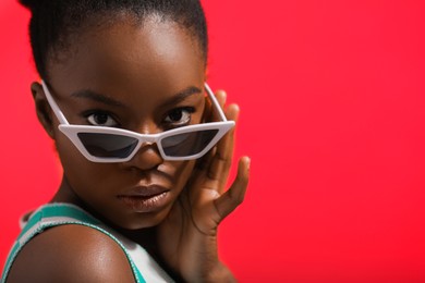 Photo of Fashionable portrait of beautiful woman with stylish sunglasses on coral background, closeup. Space for text