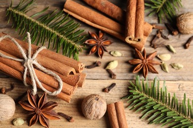 Different aromatic spices and fir branches on wooden table, flat lay