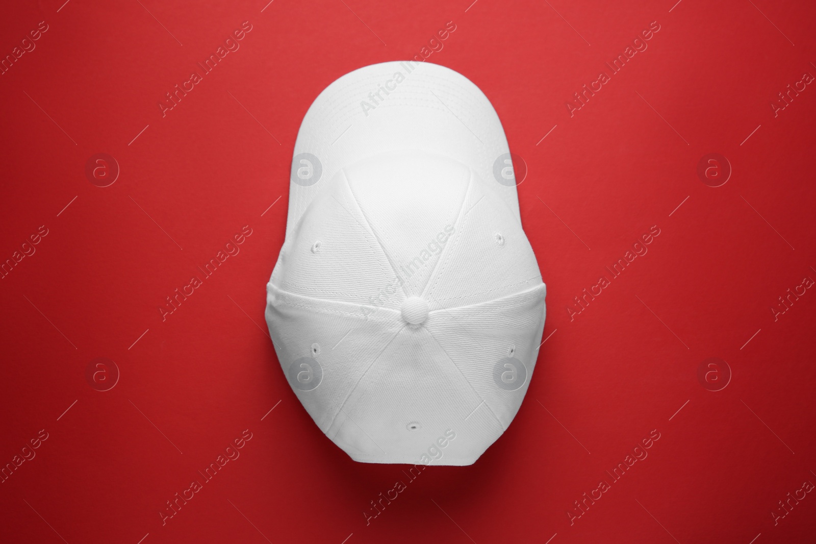 Photo of Stylish white baseball cap on red background, top view