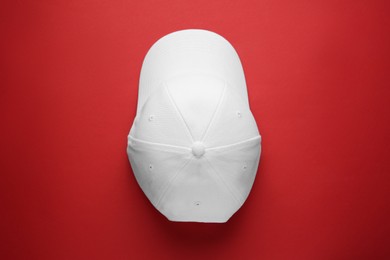 Stylish white baseball cap on red background, top view