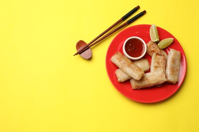 Photo of Tasty fried spring rolls, lime and sauce served on yellow table, top view. Space for text