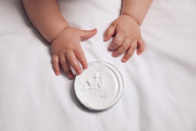 Photo of Cute little baby playing with jarmoisturizing cream on bed, closeup