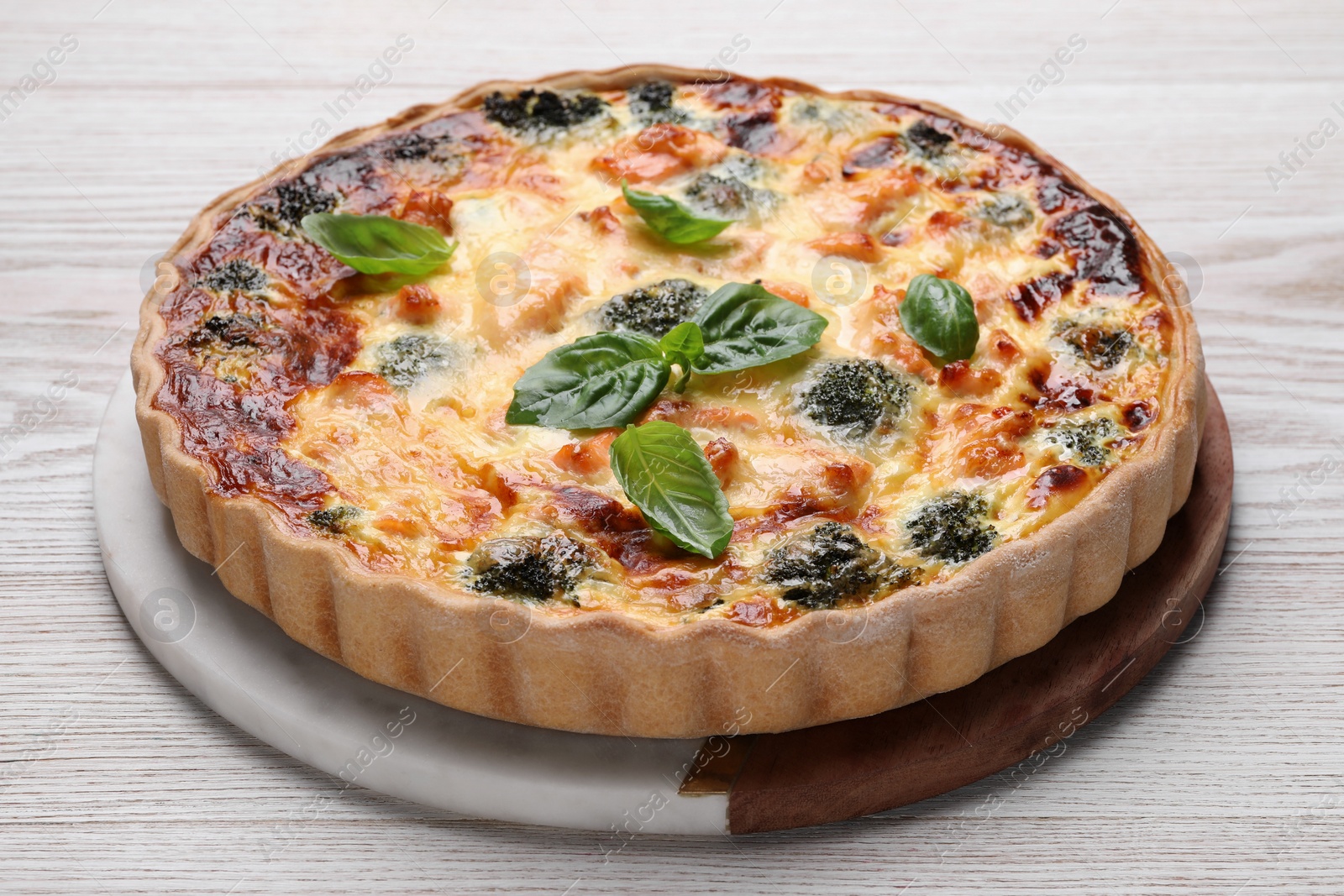 Photo of Delicious homemade quiche with salmon, broccoli and basil leaves on wooden table