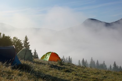 Photo of Picturesque foggy mountain landscape with camping tents in morning. Space for text