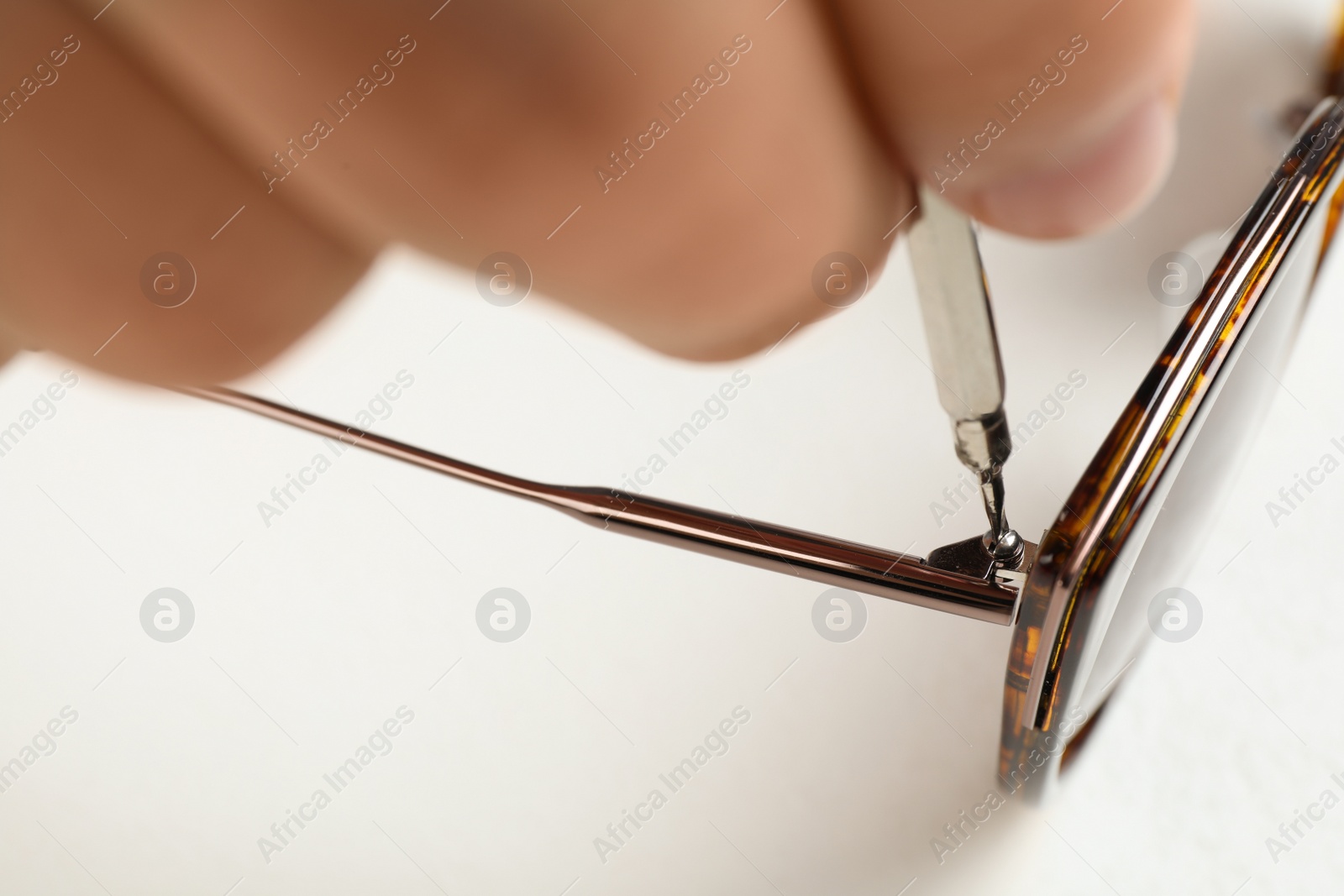 Photo of Handyman repairing sunglasses with screwdriver on white background, closeup