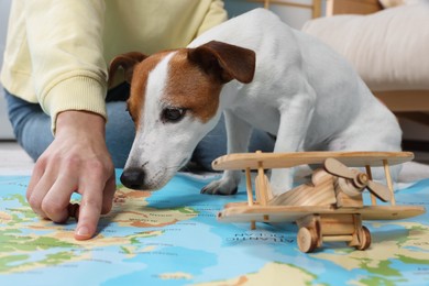 Photo of Woman pointing at location on world map near dog indoors, closeup. Travel with pet concept