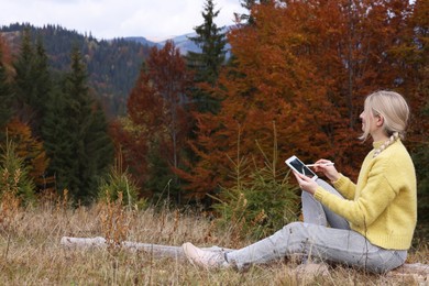 Photo of Young woman drawing with graphic tablet in mountains on autumn day