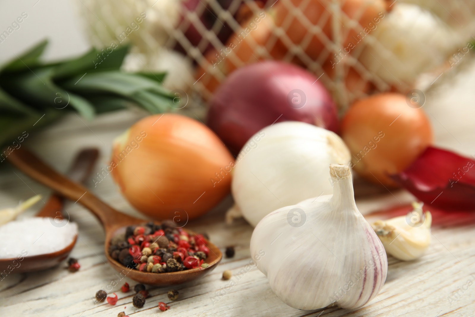 Photo of Fresh onion bulbs, leek, garlic, peppers mix and salt on white wooden table, closeup