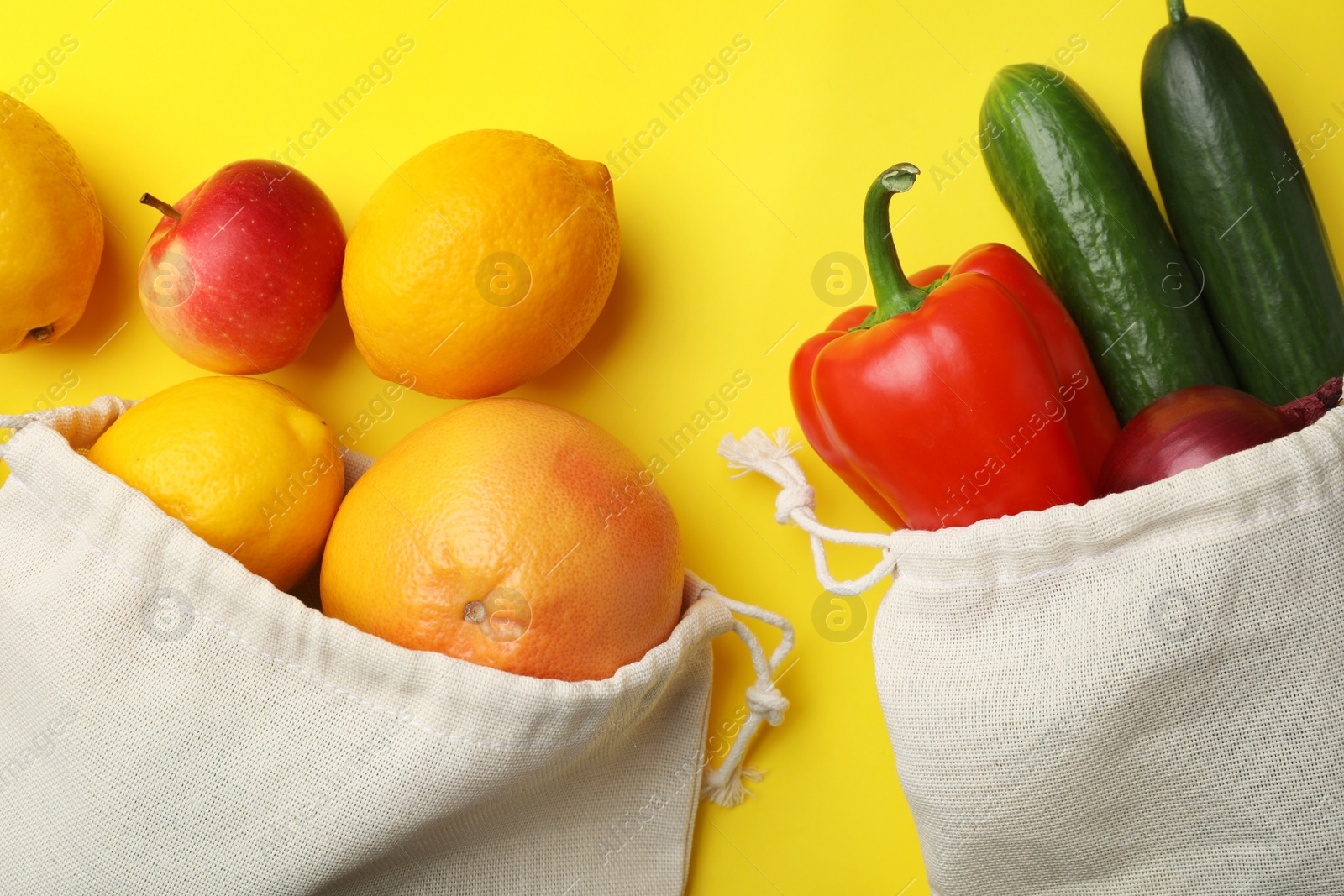 Photo of Cotton eco bags with fruits and vegetables on yellow background, flat lay