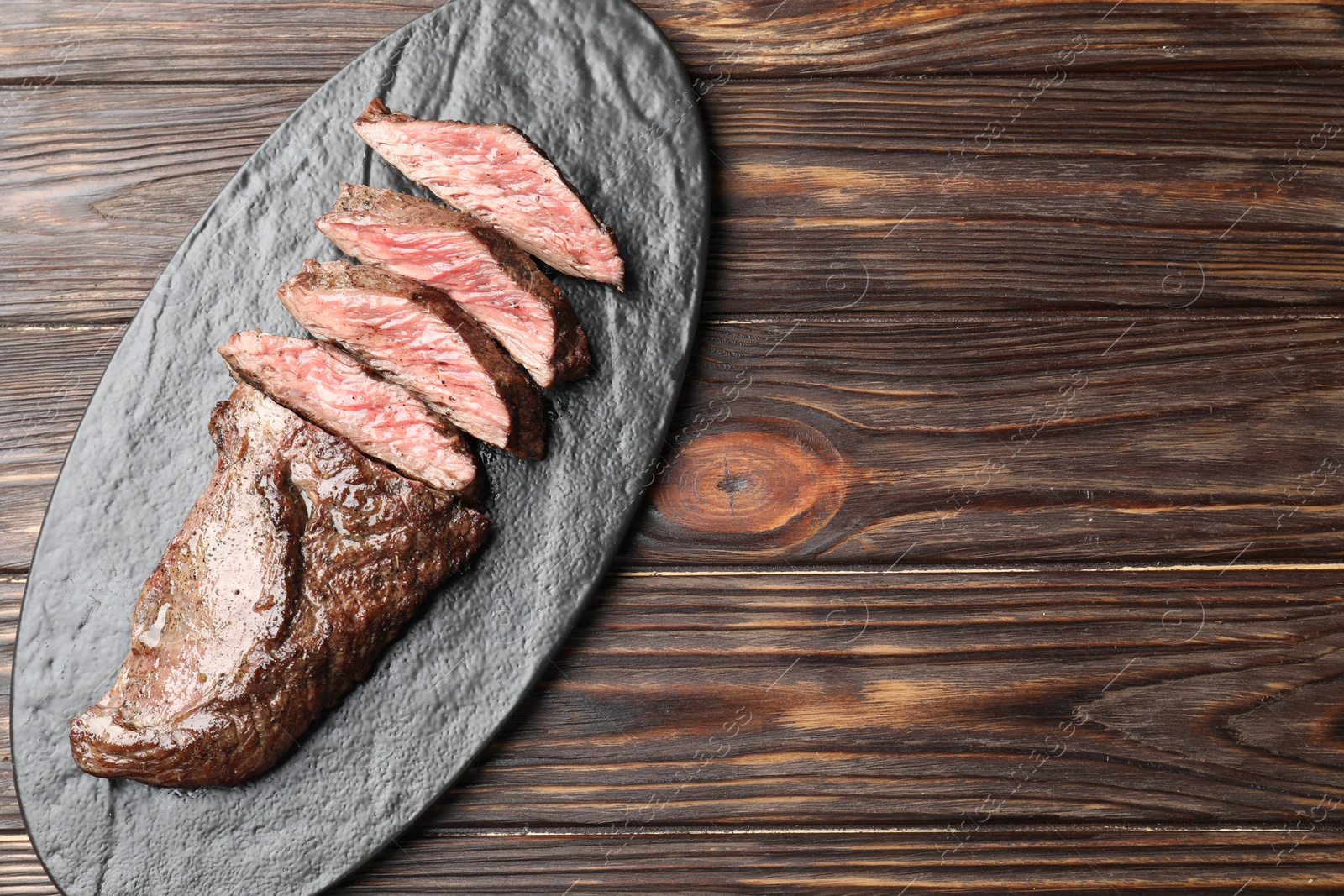 Photo of Pieces of delicious grilled beef meat on wooden table, top view. Space for text