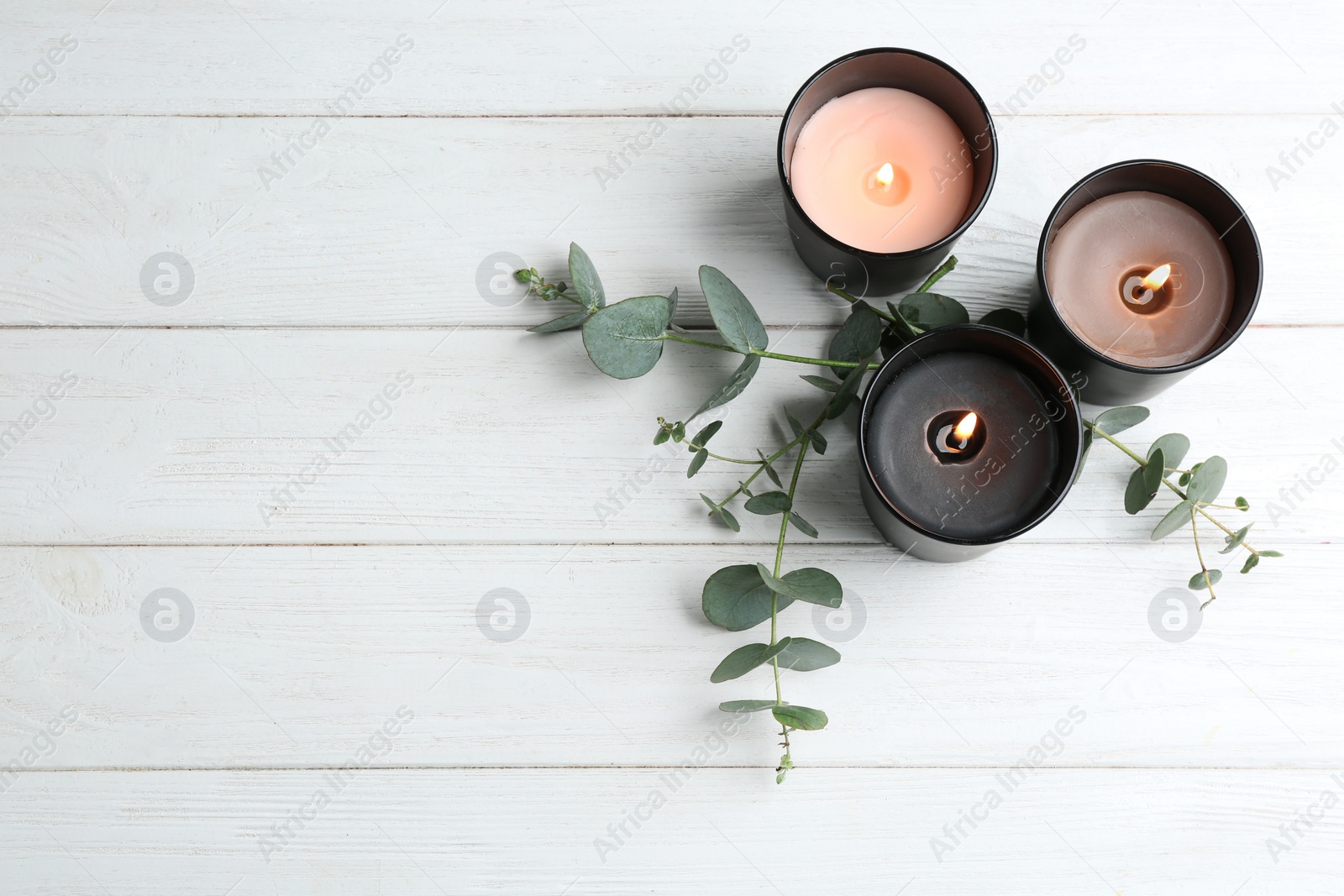 Photo of Burning candles and green branches on white wooden table, flat lay. Space for text
