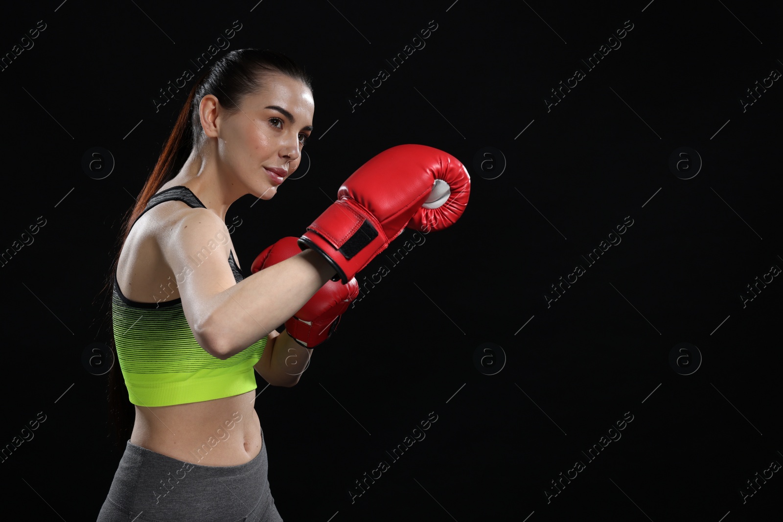 Photo of Beautiful woman in boxing gloves training on black background. Space for text