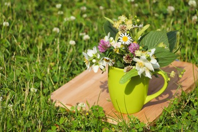 Green cup with different wildflowers and herbs on wooden board in meadow. Space for text