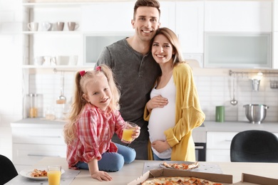 Pregnant woman and her family eating pizza in kitchen