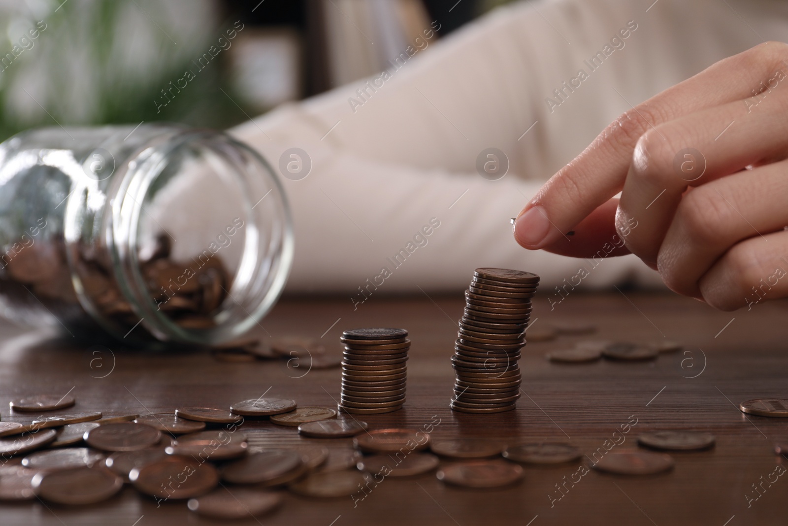 Photo of Woman stacking coins at wooden table indoors, closeup