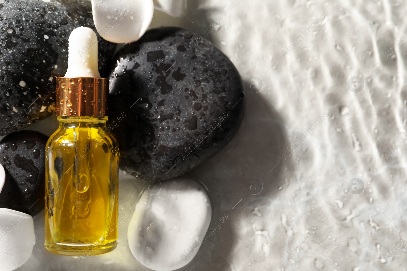 Photo of Bottle of face serum and spa stones in water on light background, flat lay. Space for text