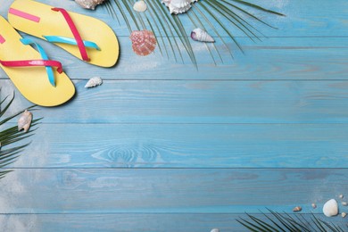 Photo of Stylish flip flops and beach objects on light blue wooden background, flat lay. Space for text