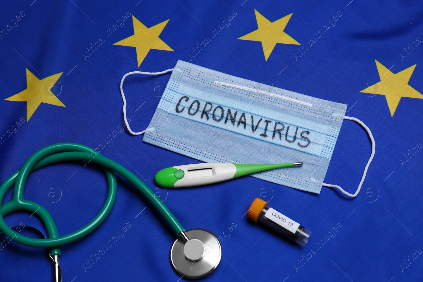 Photo of Stethoscope, medical mask with word Coronavirus, thermometer and test tube on flag of European Union