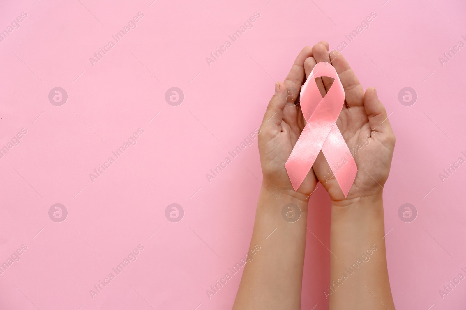 Photo of Woman holding symbolic ribbon of breast cancer awareness on color background, top view. Gynecological care