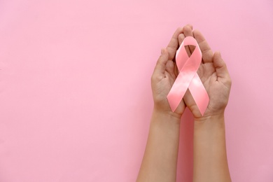 Woman holding symbolic ribbon of breast cancer awareness on color background, top view. Gynecological care