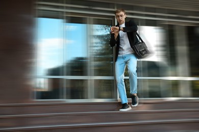 Image of Being late. Young man checking time while running down stairs outdoors. Motion blur effect