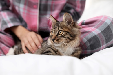 Photo of Woman wearing pajama with cat on bed, closeup. Owner and pet