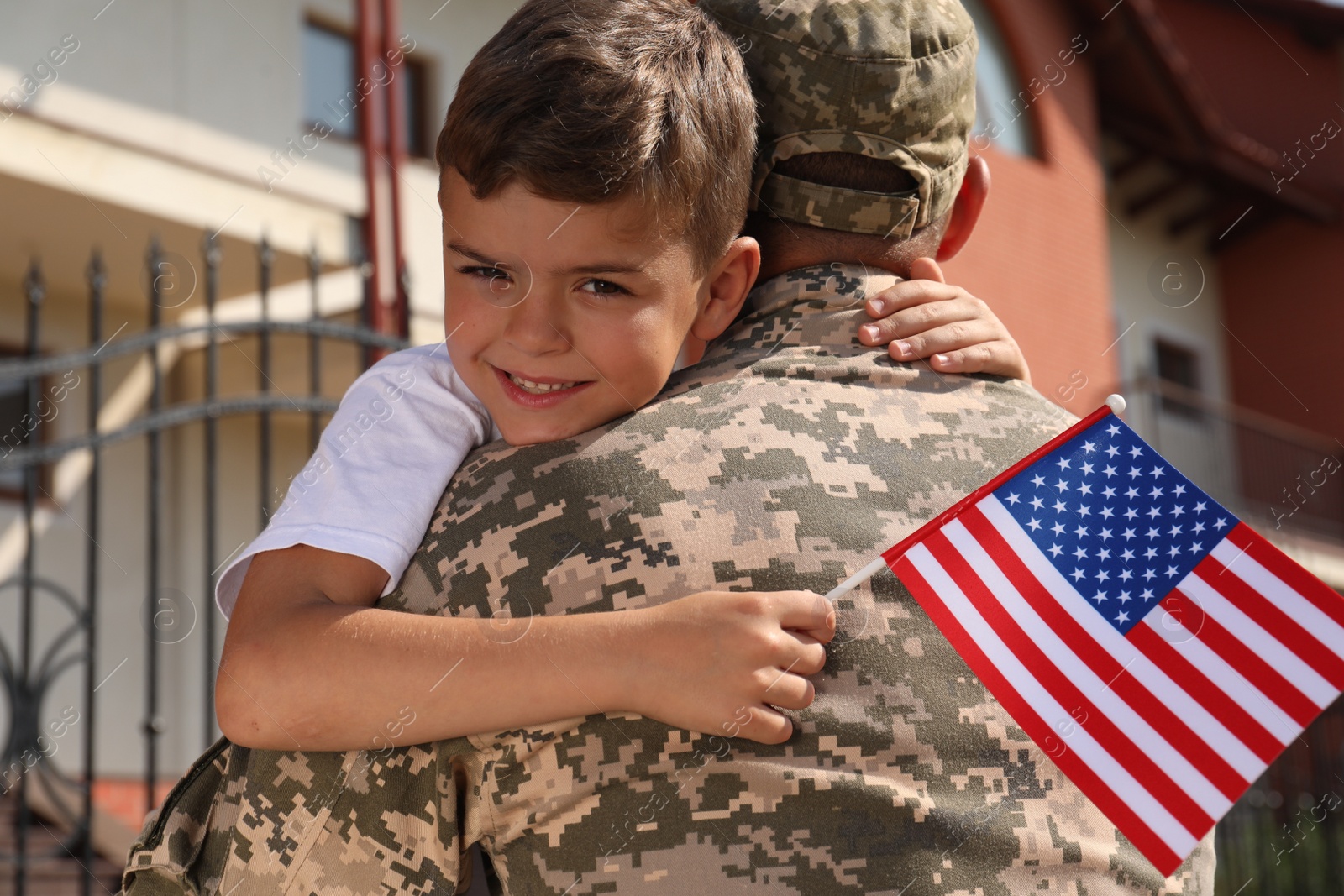 Photo of Soldier and his little son with flag of USA hugging outdoors