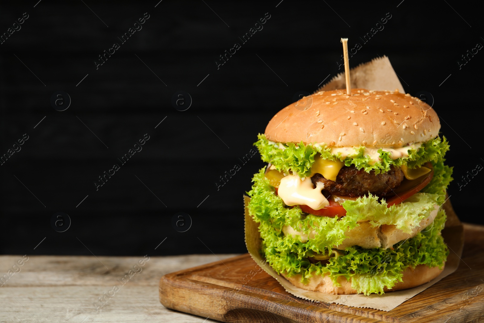 Burger with delicious patty on wooden table against dark background, space for text Photo of Burger with delicious patty on wooden table against dark background, space for text