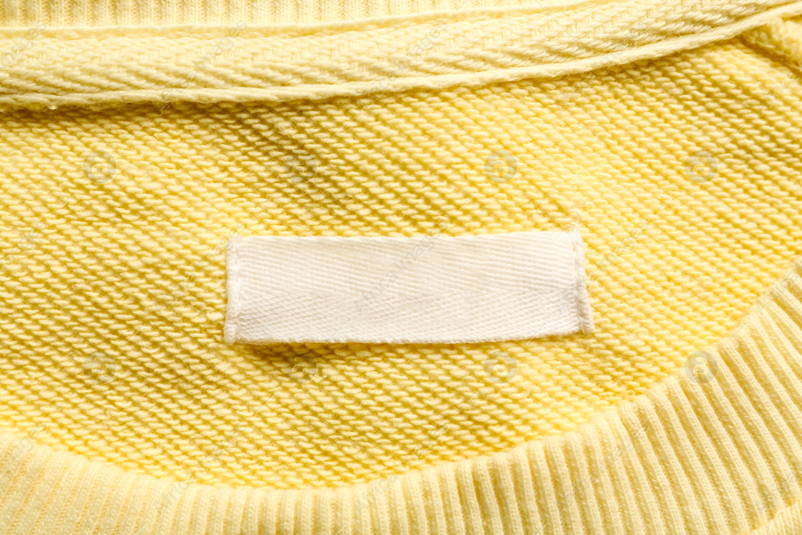 Photo of Blank clothing label on yellow sweater, top view