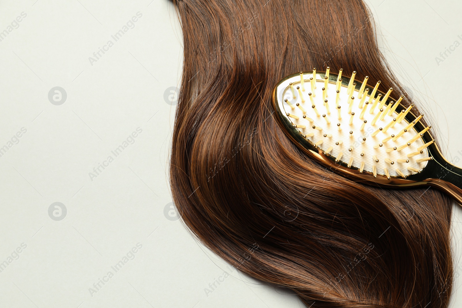 Photo of Stylish brush with brown hair strand on light grey background, top view. Space for text