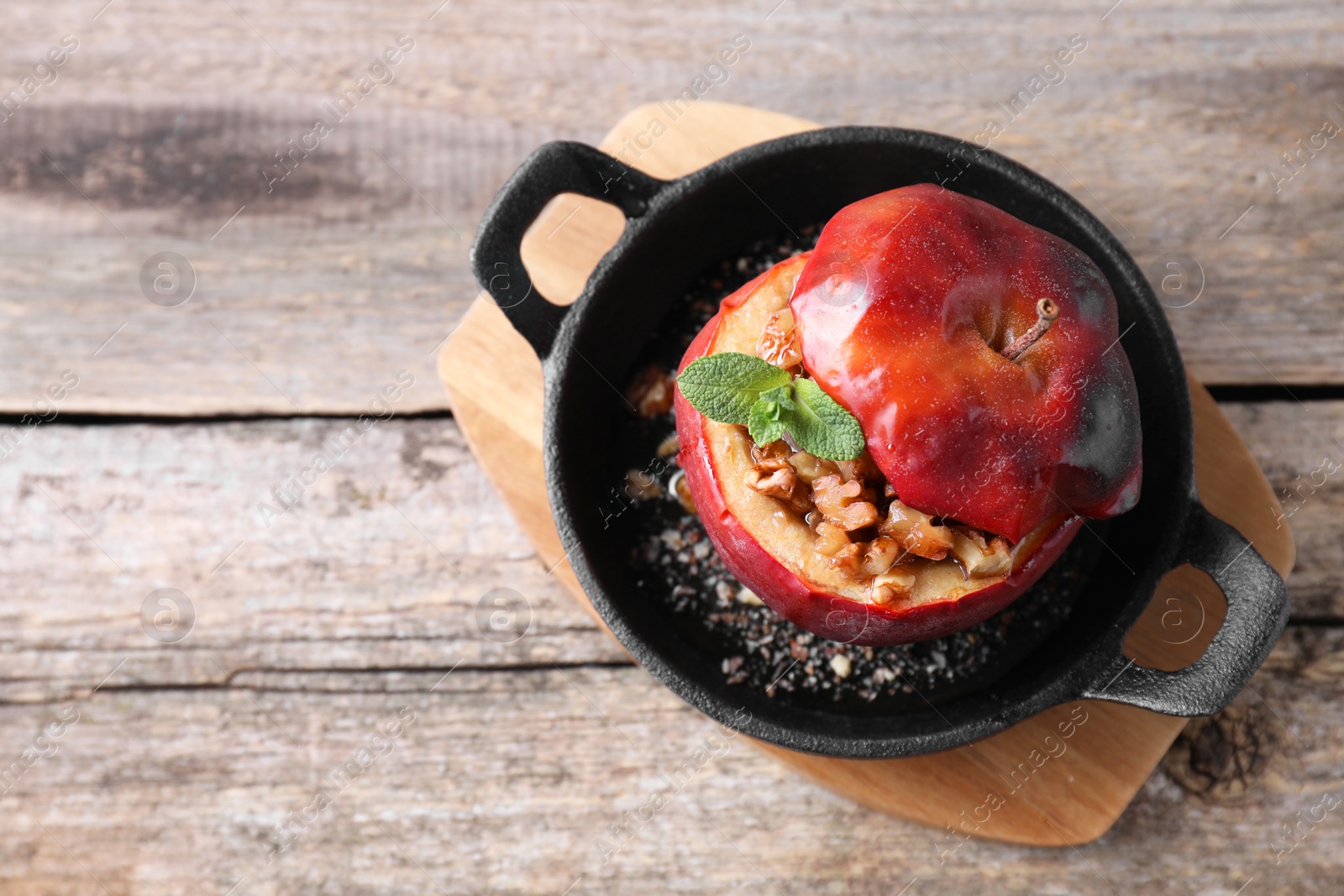 Photo of Tasty baked apple with nuts, honey and mint in baking dish on wooden table, top view. Space for text