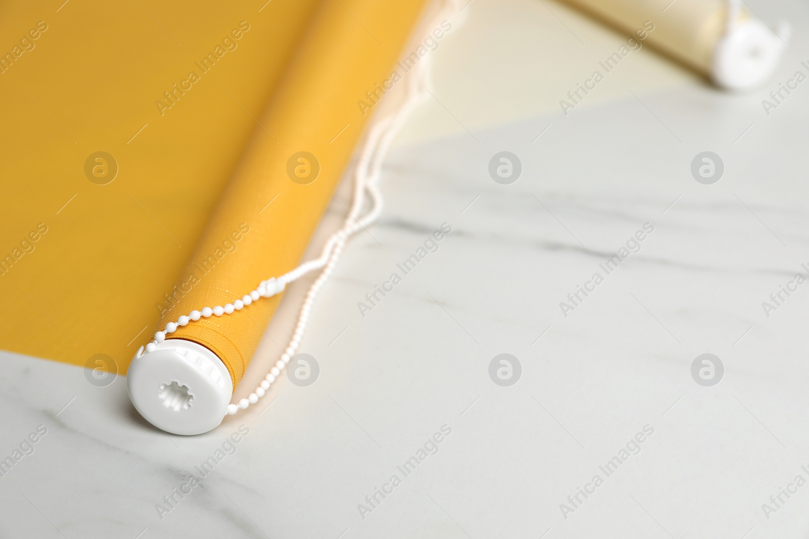 Photo of Stylish roller window blinds on white marble table, closeup. Space for text