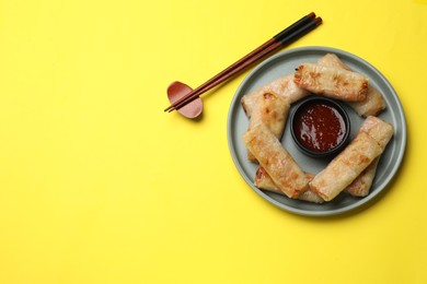 Photo of Fried spring rolls and sauce served on yellow table, top view. Space for text