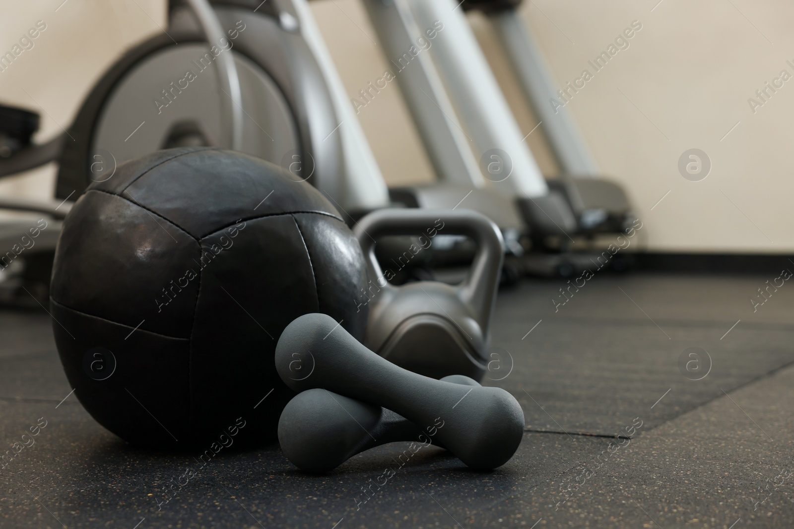 Photo of Black medicine ball, kettlebell and dumbbells on floor in gym, space for text
