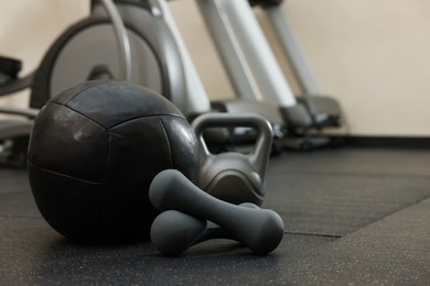 Photo of Black medicine ball, kettlebell and dumbbells on floor in gym, space for text