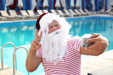 Photo of Authentic Santa Claus taking selfie near swimming pool outdoors