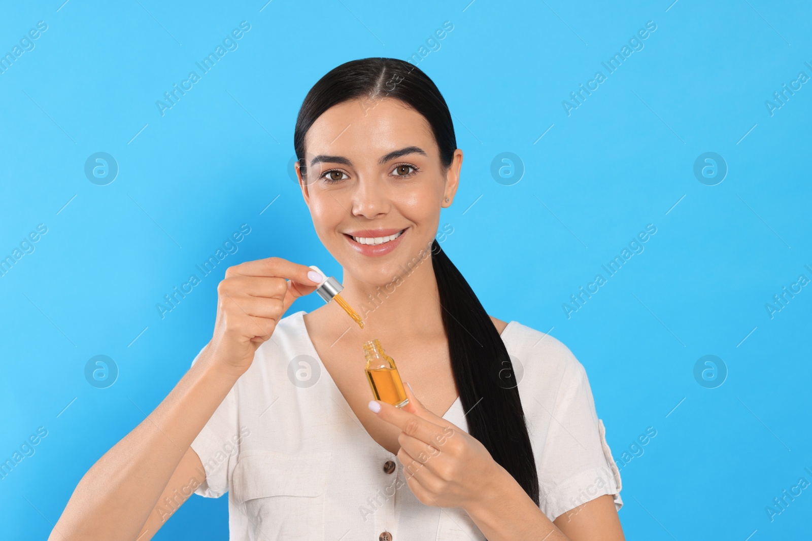 Photo of Young woman with bottle of essential oil on light blue background