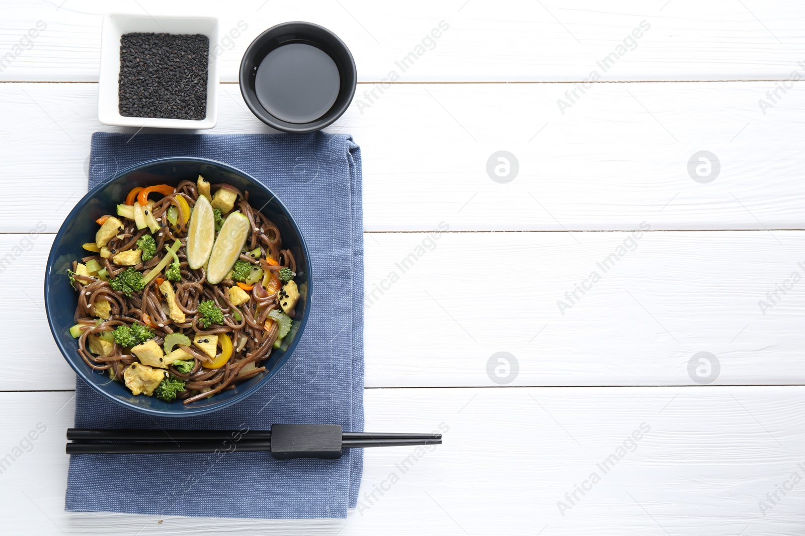 Photo of Stir-fry. Delicious cooked noodles with chicken and vegetables in bowl served on white wooden table, flat lay. Space for text