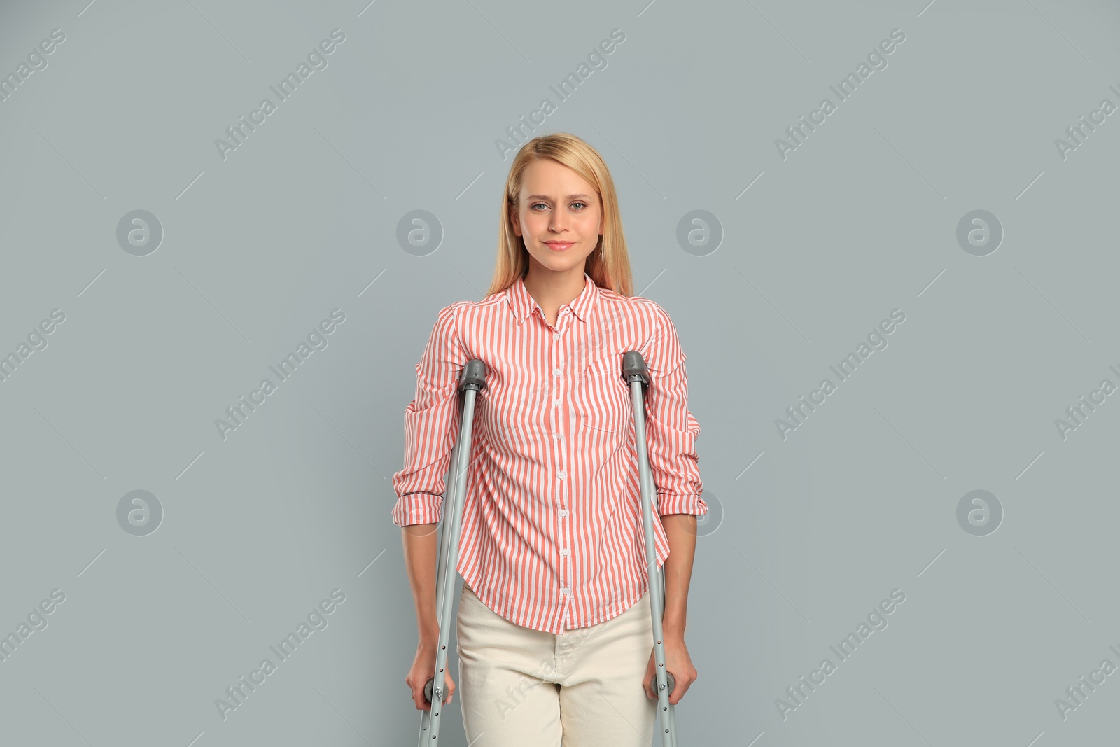 Photo of Young woman with axillary crutches on grey background