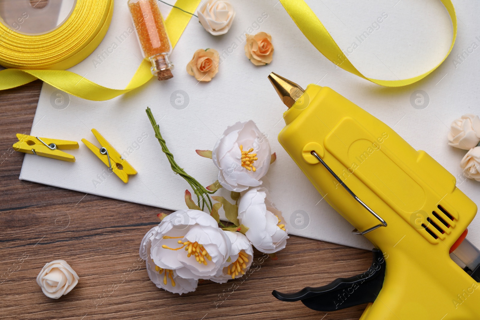 Photo of Hot glue gun and handicraft materials on wooden table, flat lay