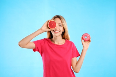 Photo of Woman choosing between doughnut and healthy grapefruit on light blue background