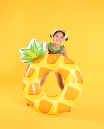 Cute little child in beachwear with bright inflatable ring on yellow background