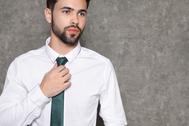 Photo of Portrait of businessman straightening tie on grey background, closeup. Space for text