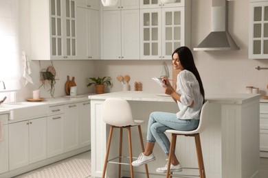 Photo of Beautiful young woman with notebook sitting on stool in kitchen