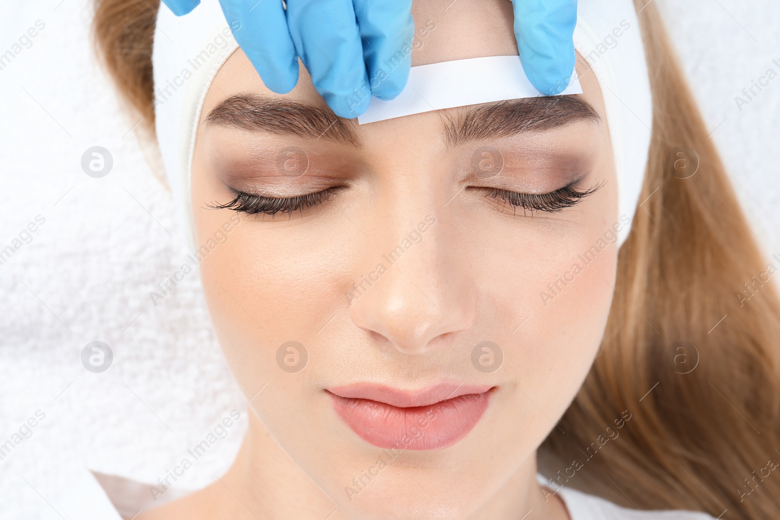 Photo of Young woman having professional eyebrow correction procedure in beauty salon