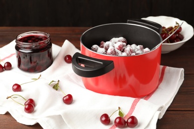 Photo of Pot with cherries and sugar on wooden table. Making delicious jam