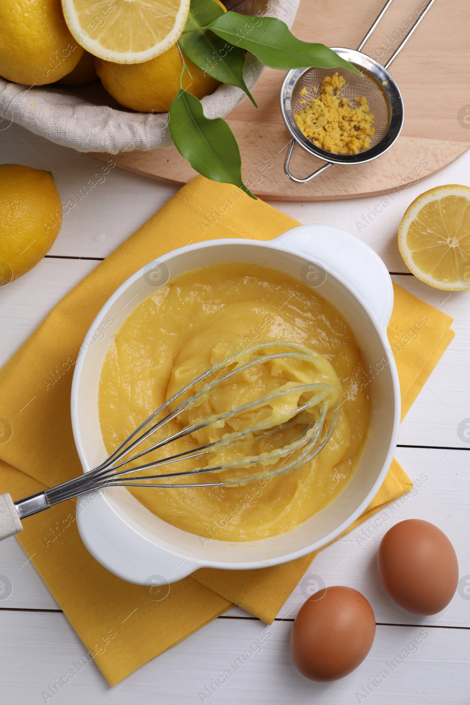 Photo of Delicious lemon curd in bowl, ingredients, whisk and sieve on white wooden table, flat lay